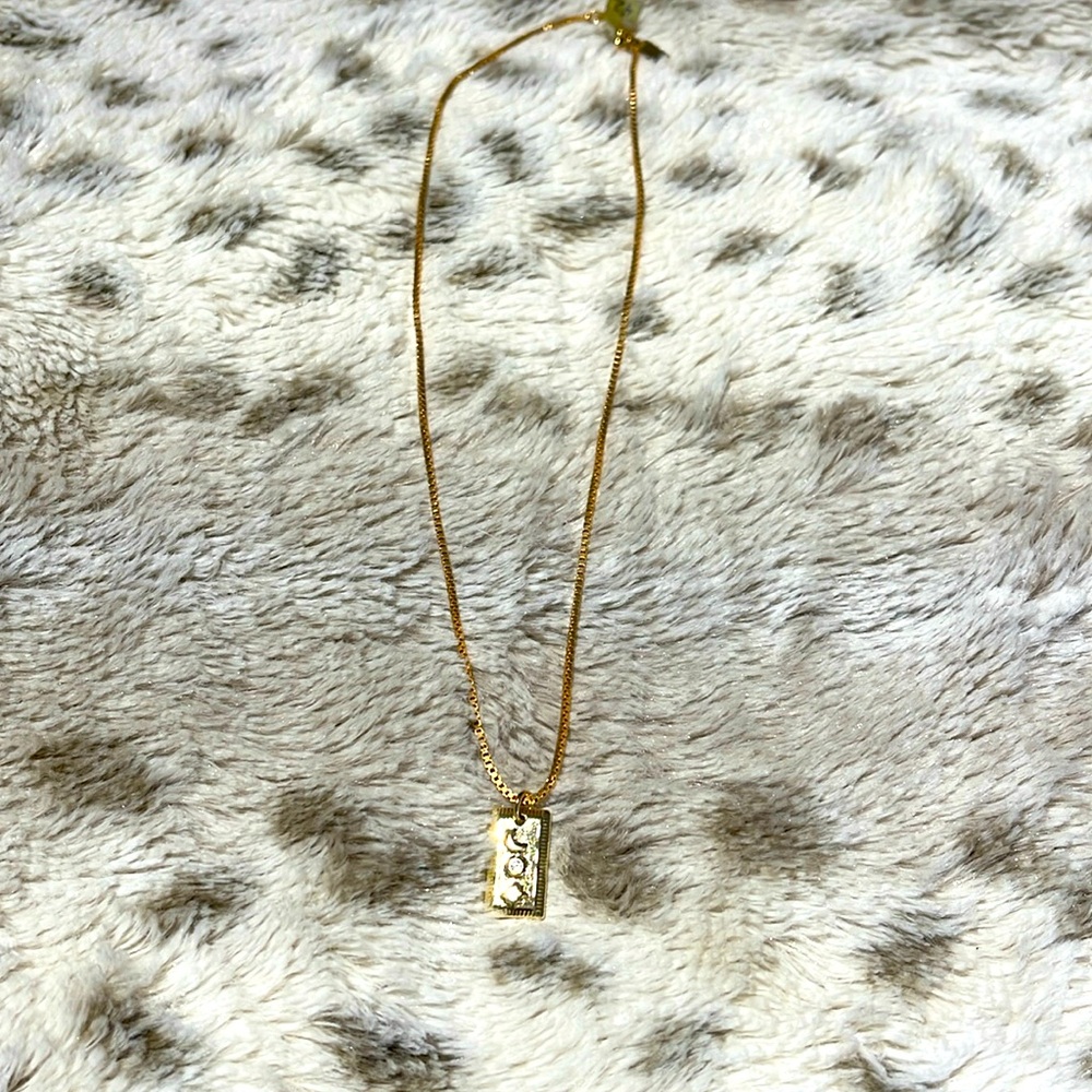 Gold necklace with rectangle pendant featuring sun, moon and star